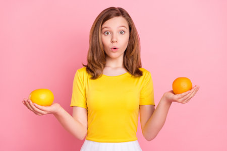 Photo of impressed brown hair teenager girl hold oranges wear yellow t-shirt isolated on pink color...