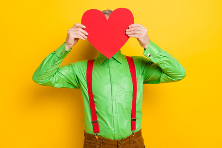 Photo of senior man incognito anonymous close face heart surprise valentine day isolated over yellow color backgroundの写真素材