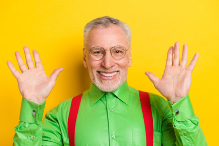 Photo portrait old man smiling in glasses waving hands greeting isolated bright yellow color backgroundの写真素材
