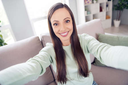 Photo of pretty shiny mature lady wear teal pullover smiling sitting couch recording video indoors house roomの写真素材