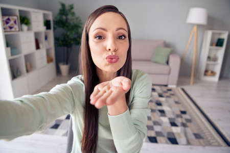 Self-portrait of attractive amorous woman staying safe sending air blow kiss feelings at home...