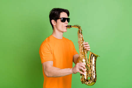Photo of joyful happy positive young man good mood hold hands saxophone player isolated on green color backgroundの写真素材