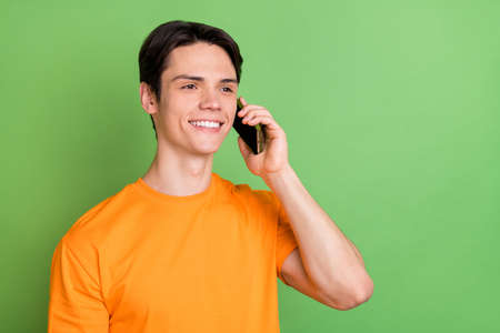 Photo of young cheerful happy dreamy man look empty space talk phone smile isolated on green color backgroundの写真素材