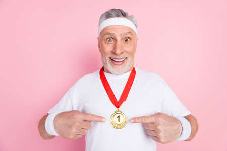 Photo of crazy sporty grandpa point medal wear white t-shirt isolated on pastel pink color backgroundの写真素材
