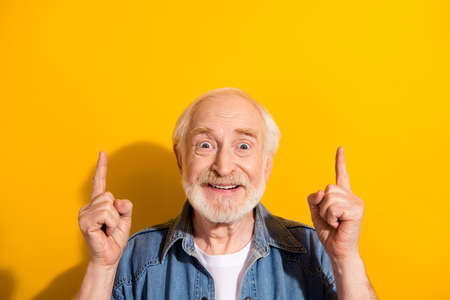 Photo of astonished cheerful man beaming smile direct fingers up empty space isolated on yellow color backgroundの写真素材