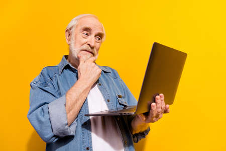 Photo of minded thoughtful old man hold hand chin look laptop interested isolated on shine yellow...