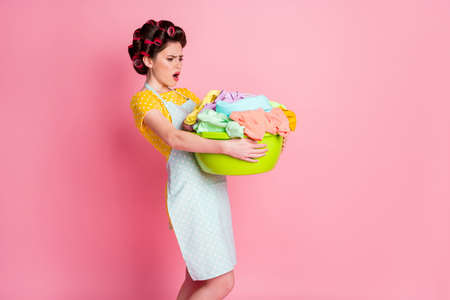 Full length photo of frustrated girl hold heavy dirty clothes basin wear yellow dotted skirt isolated pastel color backgroundの写真素材