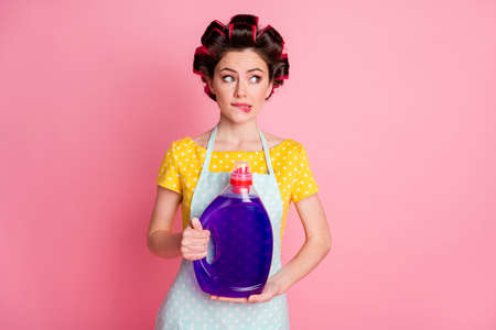 Unsure girl hold wash powder bottle bite lips look copyspace hesitate wear yellow dotted t-shirt isolated pastel color backgroundの写真素材