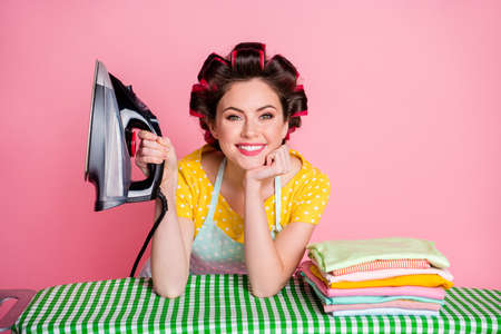 Positive maid touch hand face hold iron board dry pile clothes wear dotted t-shirt isolated pastel color backgroundの写真素材
