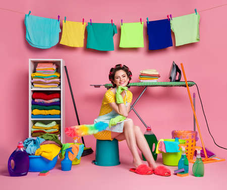 Full body view of pretty cheerful glad housemaid sitting on bucket doing clean-up isolated over pink pastel color backgroundの写真素材
