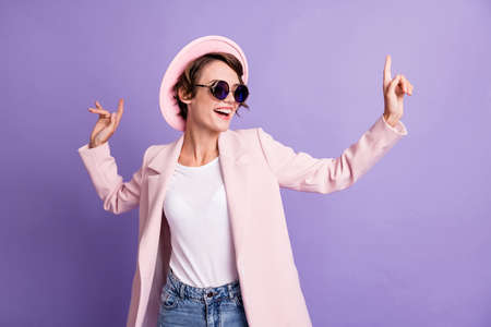 Photo of excited dance disco hit young brunette woman wear cap glasses coat isolated on purple color backgroundの写真素材