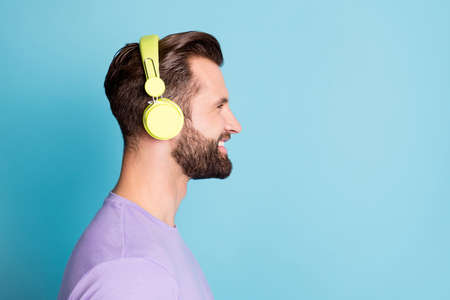 Side profile photo portrait of smiling bearded man wearing green earphones looking at blank space isolated on vivid blue color backgroundの写真素材