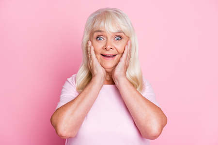Photo portrait of amazed smiling grandmother touching cheeks staring isolated on pastel pink color backgroundの写真素材