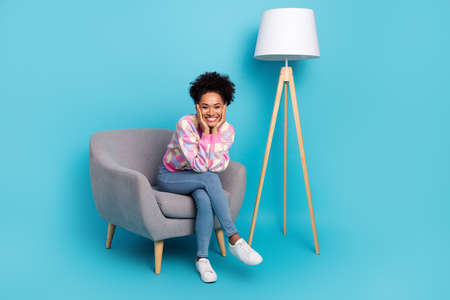 Portrait of attractive cheerful girl sitting in armchair resting free time isolated on bright blue color backgroundの写真素材