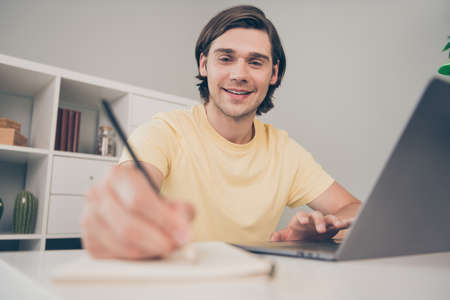Photo of cheerful nice university student guy sit desk pc write copybook wear yellow t-shirt home...