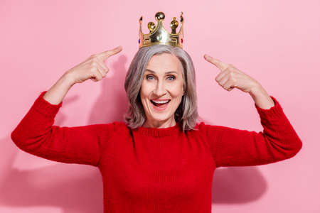 Portrait of attractive cheerful gray-haired woman celebrating demonstrating tiara isolated over pink...