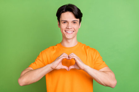 Photo of cheerful young affectionate man make fingers small heart shape smile isolated on green color backgroundの写真素材