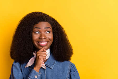 Portrait of cheerful pretty dark skin lady hand finger on chin look empty space isolated on yellow color backgroundの写真素材