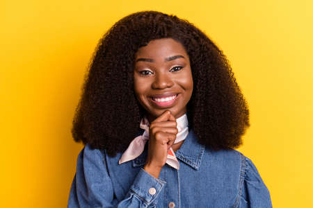 Portrait of adorable friendly dark skin girl hand finger on chin toothy smile isolated on yellow color backgroundの写真素材