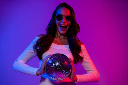 Photo of hooray millennial lady hold disco ball wearing white top eyewear isolated over gradient colorful backgroundの写真素材