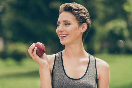 Photo of cheerful hungry healthy sportswoman eat fresh apple wear grey top nature park garden...