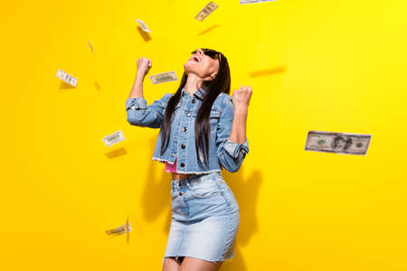 Portrait of trendy beautiful cheerful girl rejoicing 100 atm usd us faling isolated over bright yellow color backgroundの写真素材
