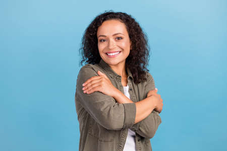 Portrait of attractive cute cheerful wavy-haired girl hugging herself isolated over bright blue...