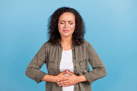 Portrait of attractive frustrated wavy-haired girl touching belly bad feeling isolated over bright blue color backgroundの写真素材