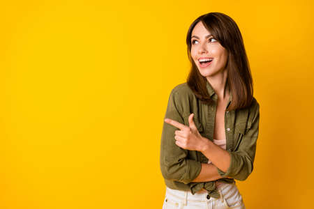 Portrait of pretty cheerful person look indicate finger empty space proposition isolated on yellow color backgroundの写真素材