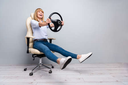 Full size photo of excited lady sit armchair ride steering wheel modern innovative game wear denim jeans isolated grey color backgroundの写真素材