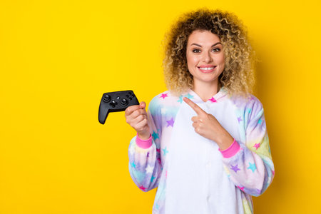 Portrait of attractive cheery wavy-haired girl in pajama demonstrating game pad pastime isolated...