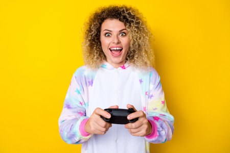 Portrait of attractive cheery crazy addicted wavy-haired girl in pajama playing console isolated over bright yellow color backgroundの写真素材