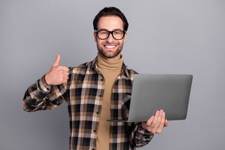Photo of confident guy dressed checkered shirt glasses communicating device thumb up isolated grey color backgroundの写真素材