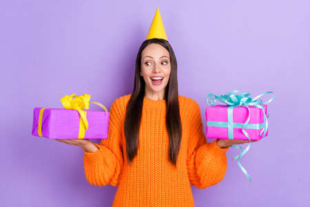 Photo of excited surprised lady hold two presents make choice wear cone cap orange sweater isolated...