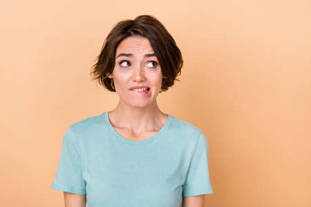 Photo of young girl worried bite lips teeth look empty space trouble isolated over beige color backgroundの写真素材