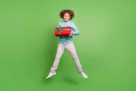 Full length body size view of attractive cheery guy jumping holding giftbox isolated over bright green color backgroundの写真素材