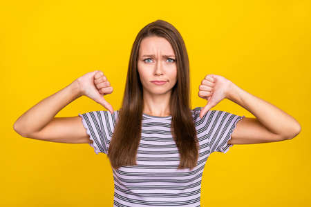 Photo of unhappy upset young woman make thumb down bad mood stressed isolated on yellow color backgroundの写真素材