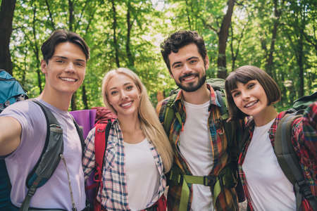 Self-portrait of attractive four cheerful people hikers exploring country world on fresh air vacation outdoorsの写真素材