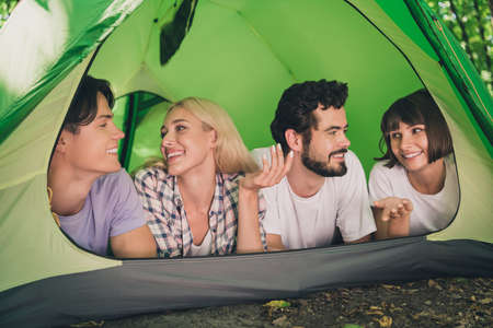 Photo portrait four friends staying in tent relaxing communicating wearing casual clothes laying in tent summer woodの写真素材