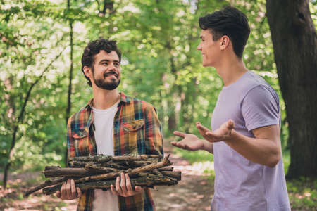 Portrait of attractive cheerful two people spending free time in wild park on fresh air looking collecting wood for setting fire outdoorsの写真素材