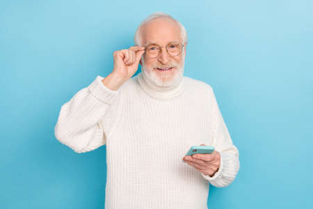 Photo of nice elder beard man hold telephone wear eyewear white turtleneck isolated on blue color...