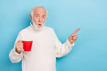 Photo of hooray aged man indicate promo hold cup wear white jumper isolated on blue color background