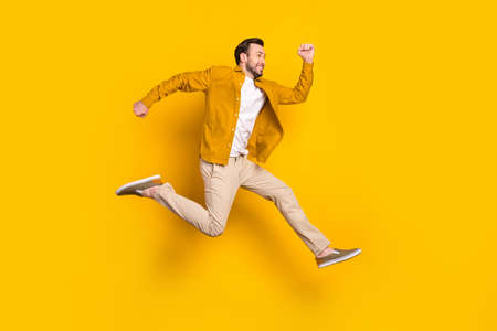 Full length photo of funky cute young guy wear casual clothes jumping running looking empty space smiling isolated yellow color backgroundの写真素材