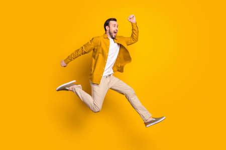 Full length photo of happy hurrying gentleman dressed casual outfit smiling jumping high running isolated yellow color backgroundの写真素材