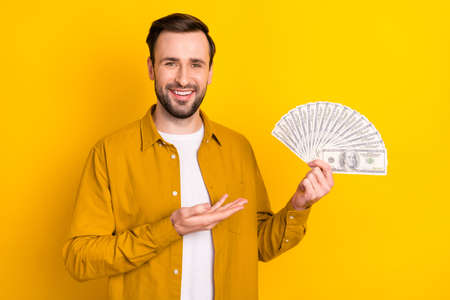 Photo of cheerful cute gentleman dressed casual outfit holding arm empty space money fan smiling...