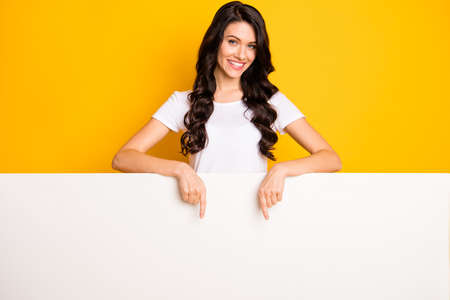 Photo of pretty adorable young woman wear white t-shirt pointing big white wall empty space isolated yellow color backgroundの写真素材