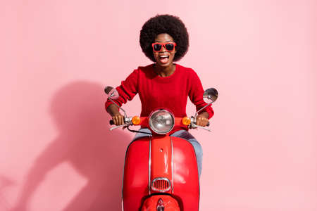 Photo of excited happy dark skin woman ride motorcycle wear sunglass isolated on pastel pink color backgroundの写真素材