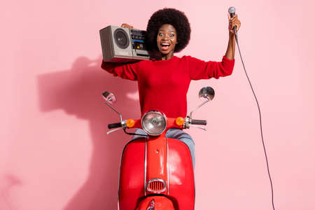 Portrait of crazy dark skin person sit on moped hold boombox mic open mouth smile isolated on pink color backgroundの写真素材
