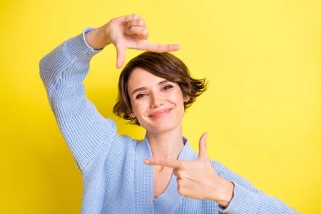Photo of photographer lady fingers show frame shape wear blue cardigan isolated yellow color backgroundの写真素材