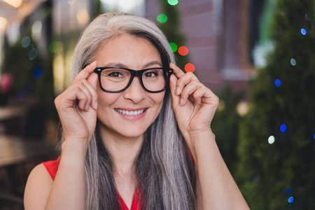 Photo of mature cheerful asian woman happy positive smile hands put eyeglasses vision summer outdoorsの写真素材